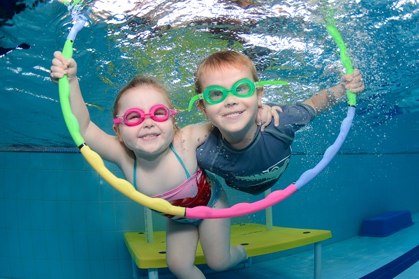 Two children swim through a rainbow hoop underwater