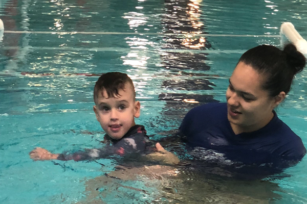 A female swim instructor assists a young boy learn to swim