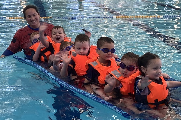 Children in life jackets floating on a pool mat